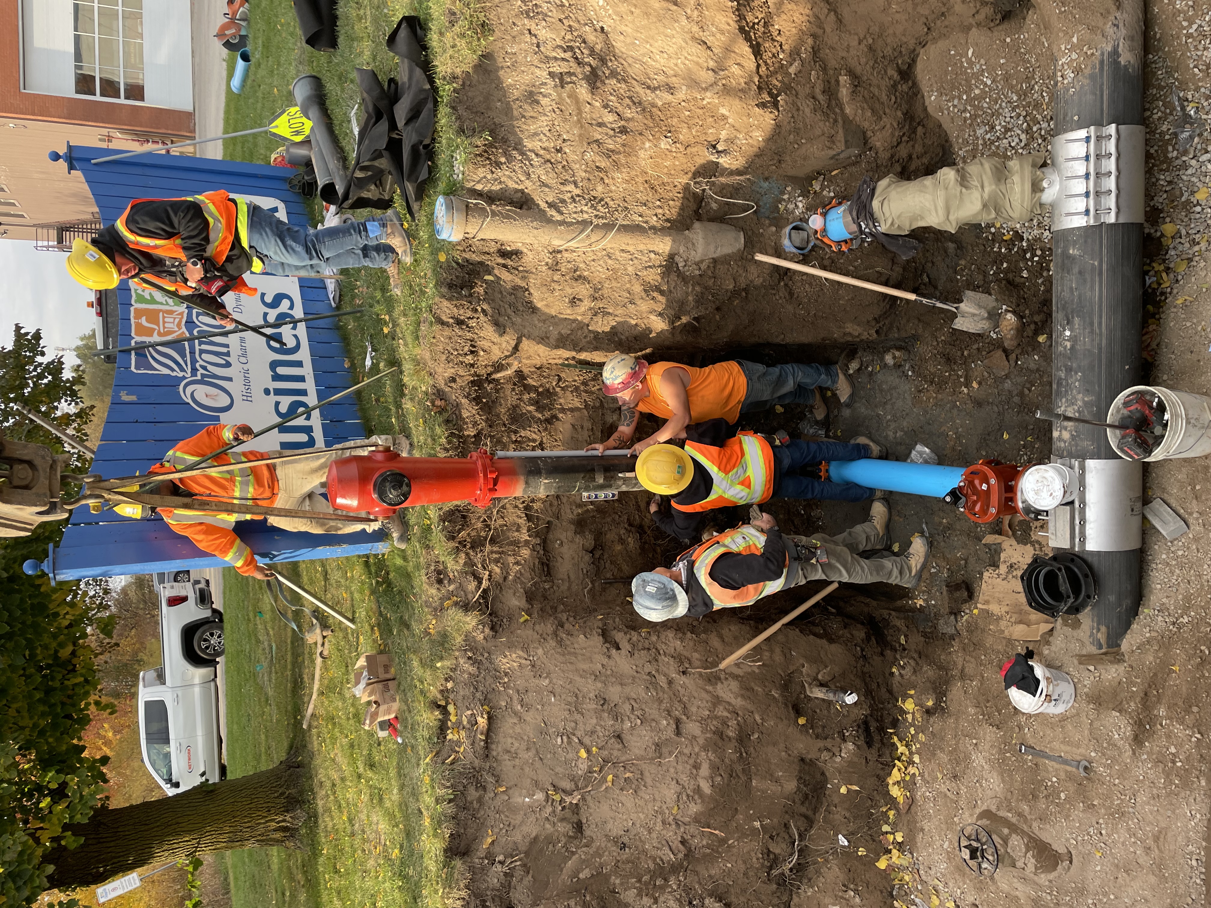 Construction workers moving a fire hydrant into place in a large hole in the ground