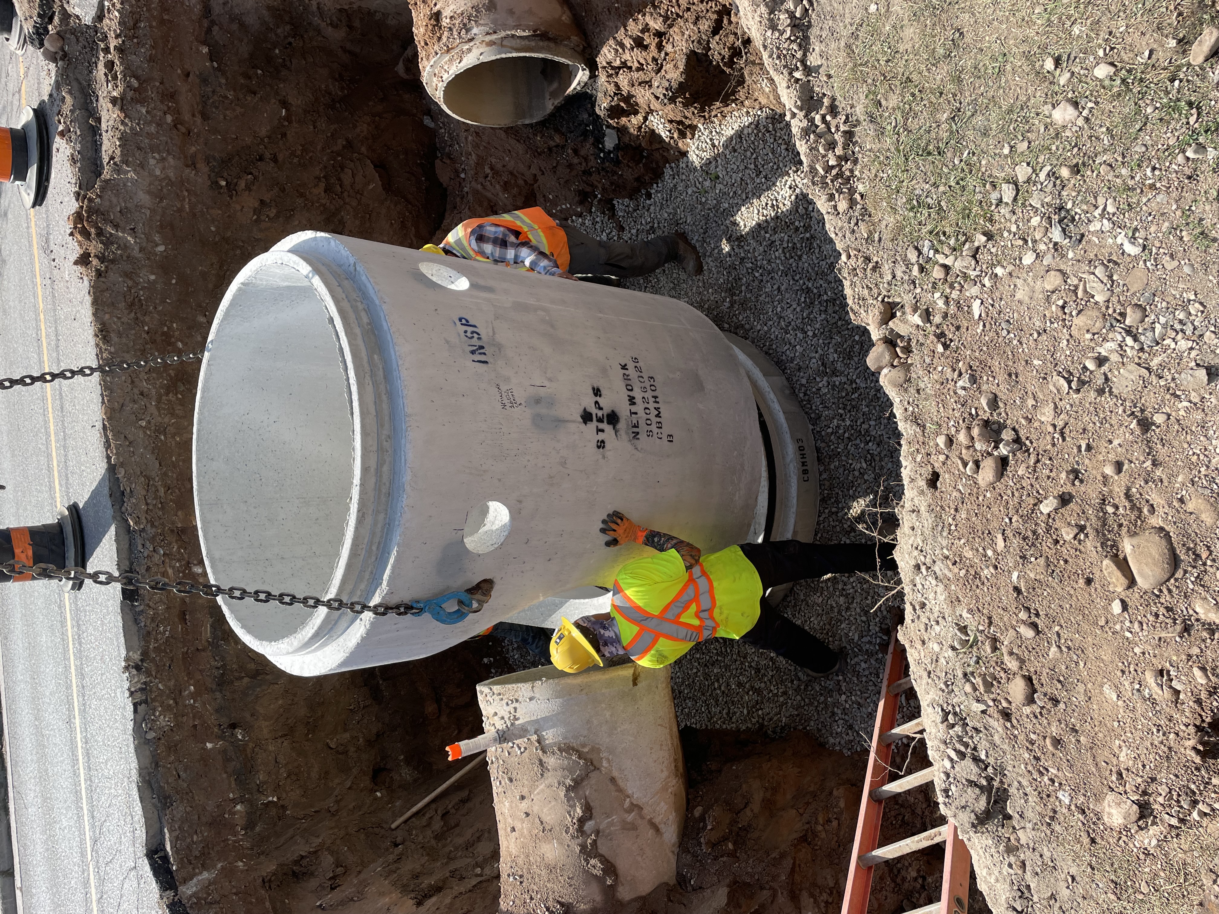 Construction workers moving a large piece of concrete into place in a large hole in the ground