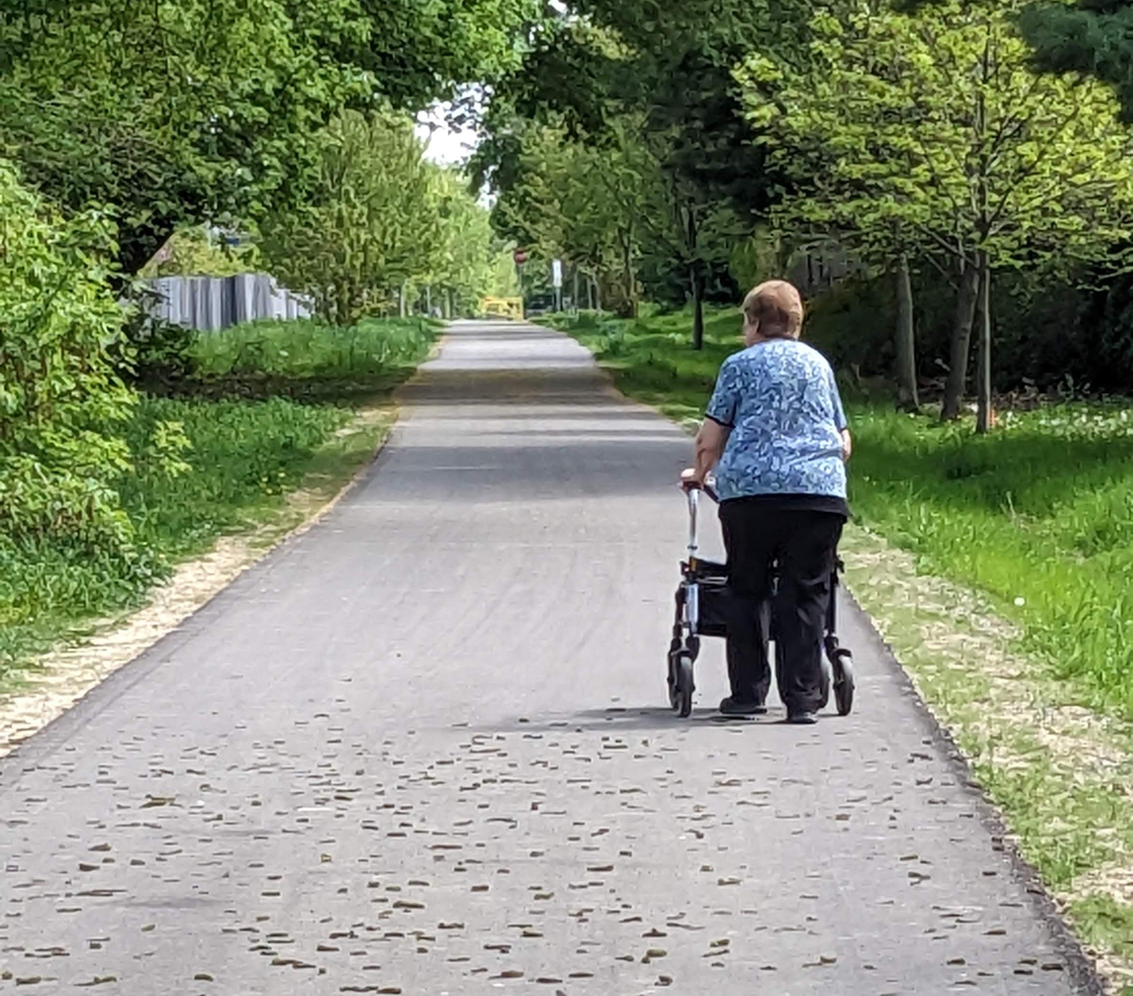 A woman walking with a walker on a paved trail