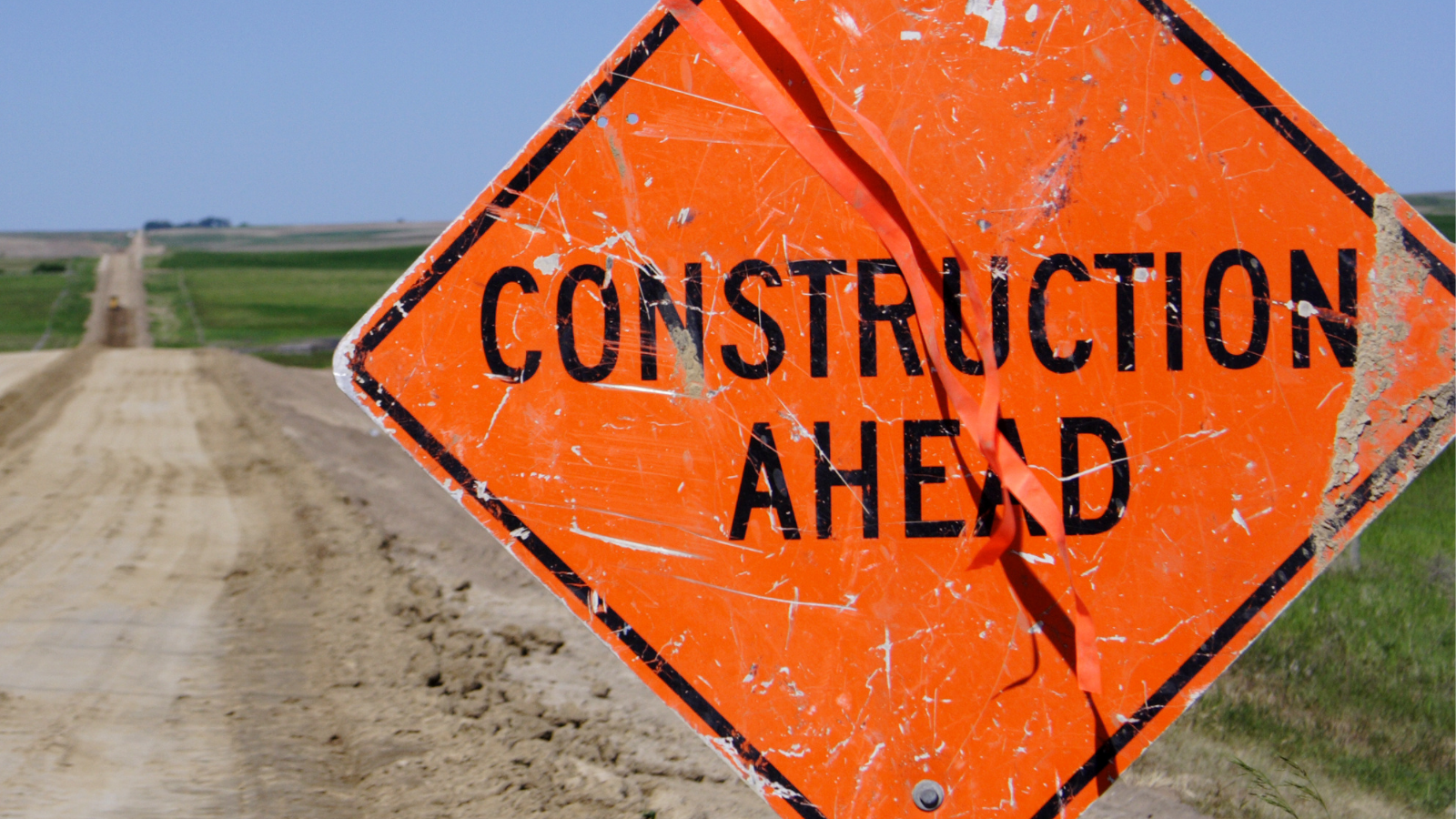 An orange "construction ahead" sign installed on the shoulder of a country road.