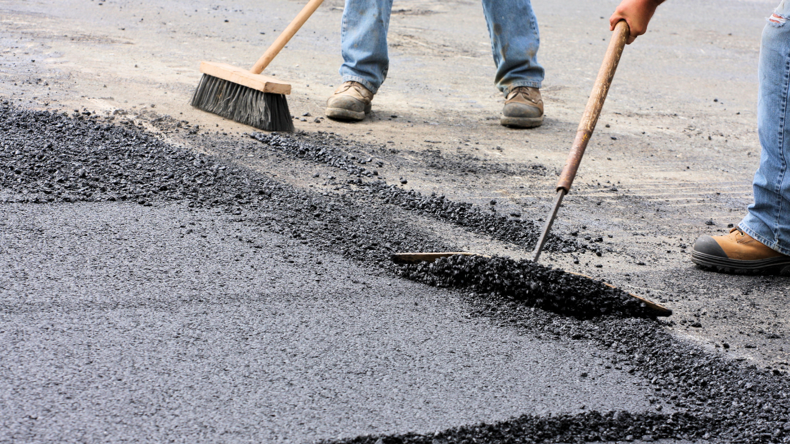 Two workers lay hot asphalt on a new roadway.