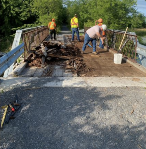 Workers fix a bridge adjacent to a trail entryway. 