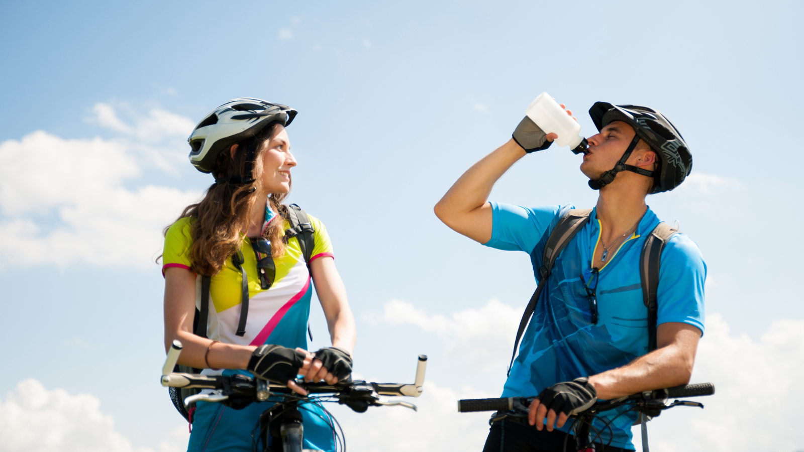 Two cyclists stop to take a drink of water. 