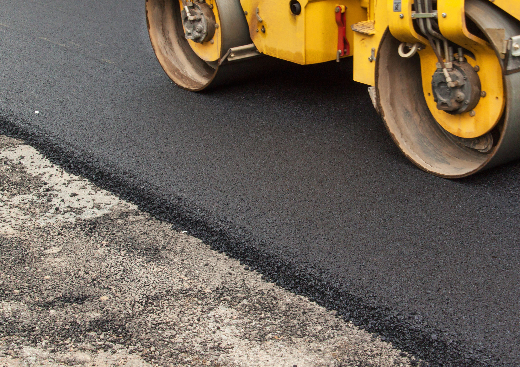 A stock image of asphalt being compacted on a roadway. 