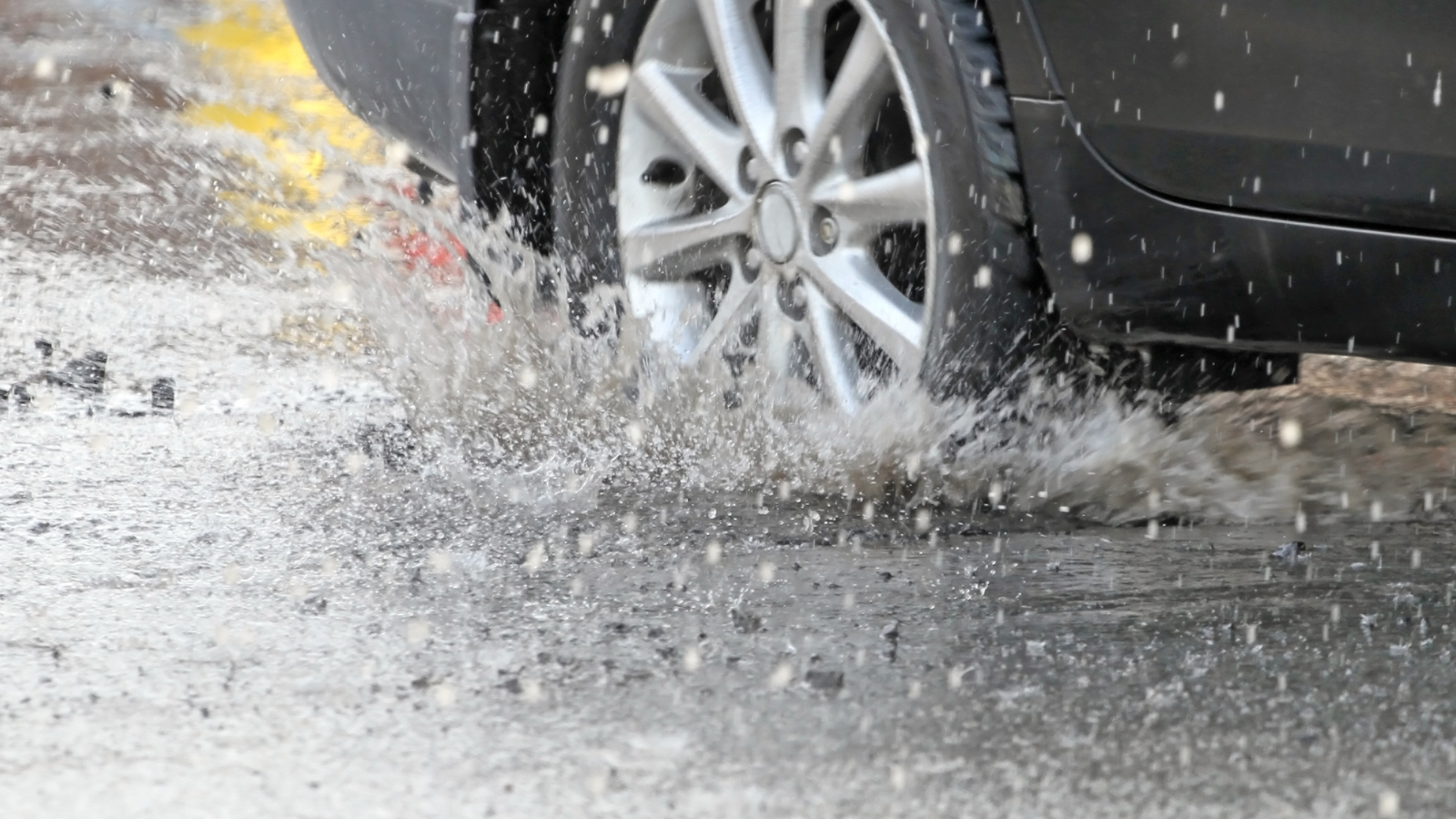 A stock image of a vehicle driving through a rainy pothole.