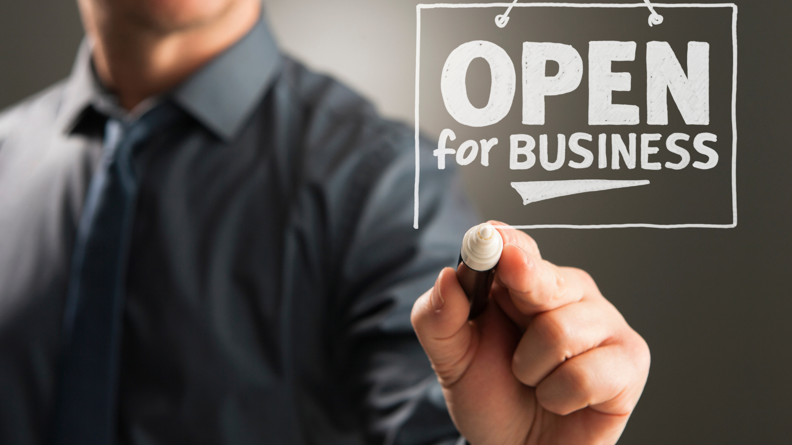 A man writing "open for business" with a white marker.