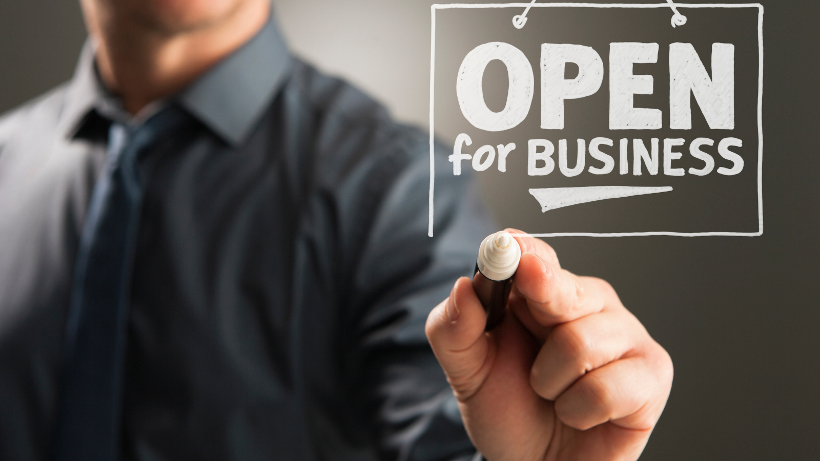 A man writing "open for business" with a white marker. 