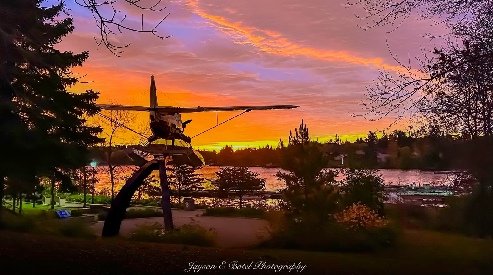 A sunset view of a statue of a plane near a lake and trees