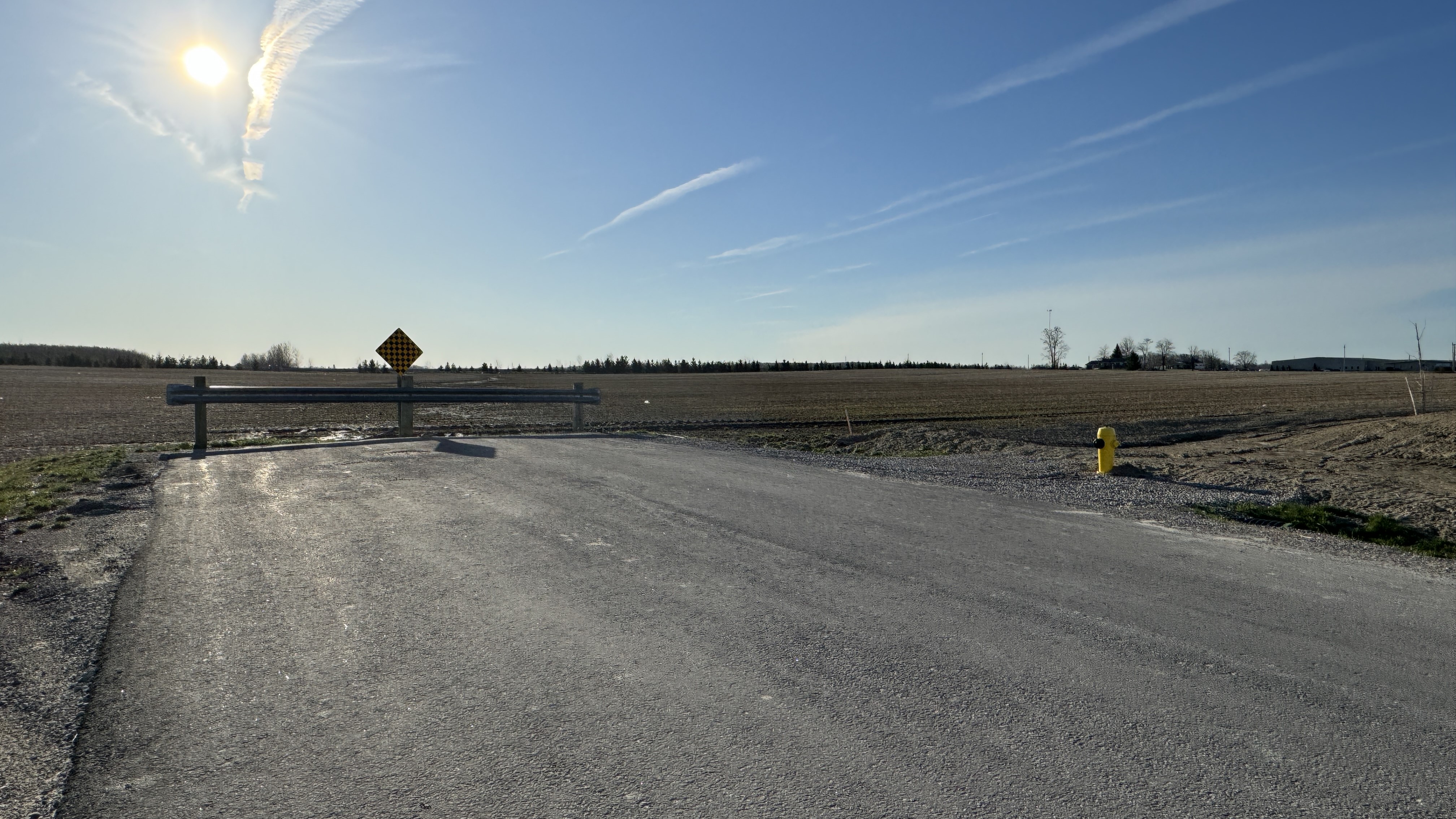 A road with a fence at the end, with grass on the other side of the fence. 