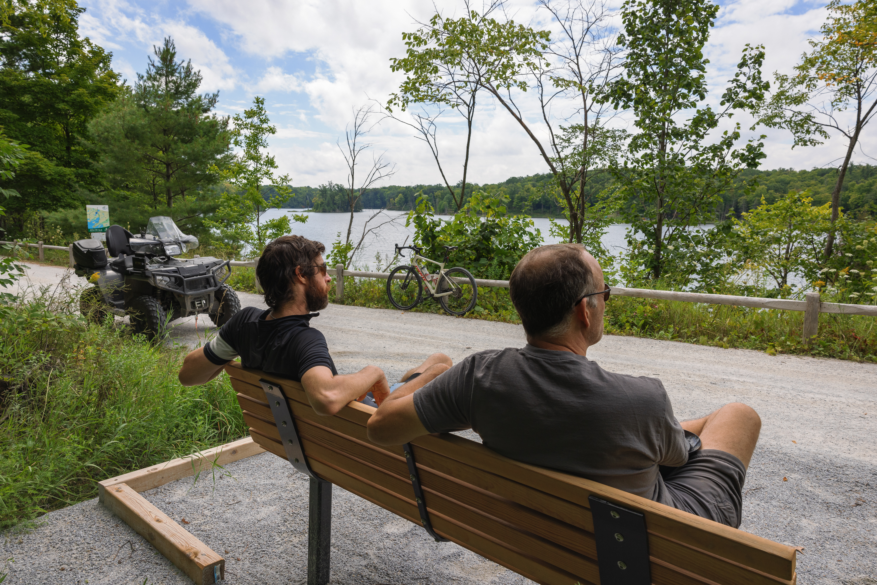 Two people sitting on a bench by a trail