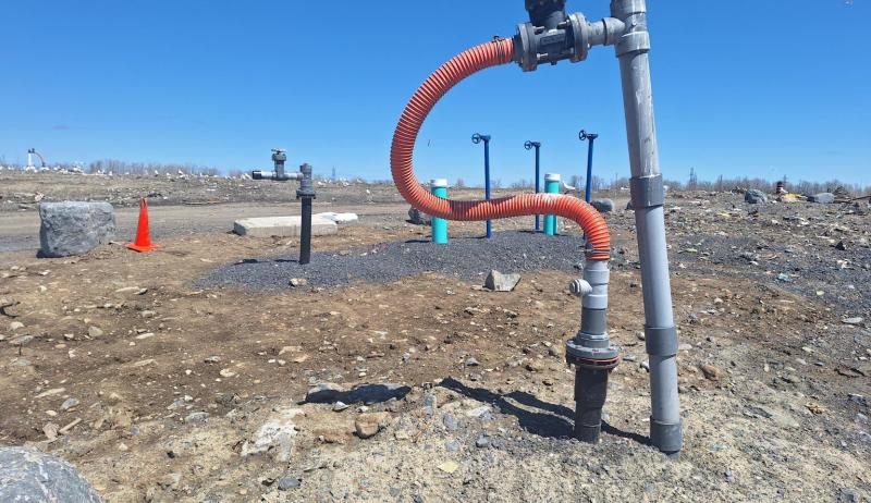 A pipe coming out of the rocky top layer of a landfill