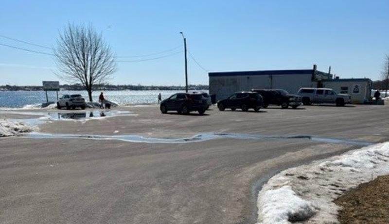 The photo shows a parking lot on a sunny winter day next to a lake. 