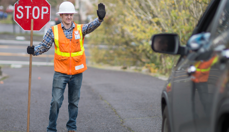 A stock image of a construction worker holding a stop sign and directing traffic. 