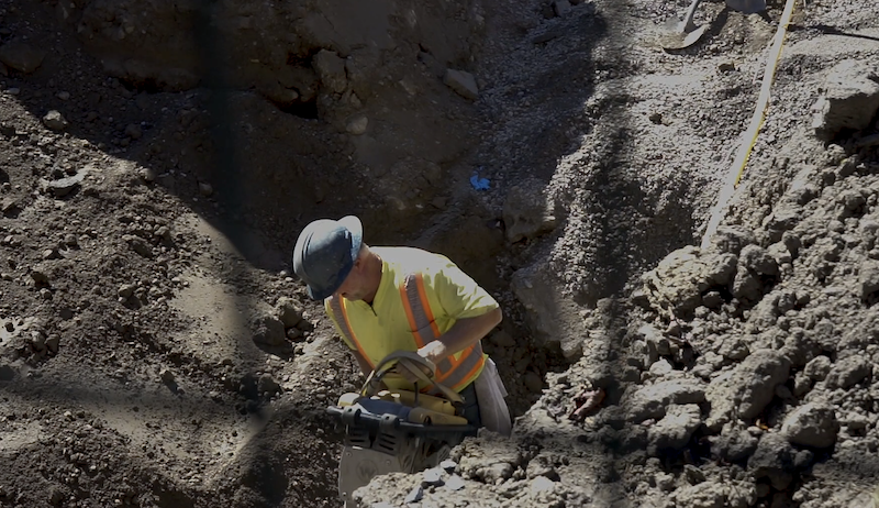 A construction worker compacting dirt in a hole. 