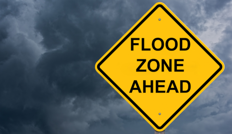 A stock image of a yellow sign that reads "flood zone ahead". 