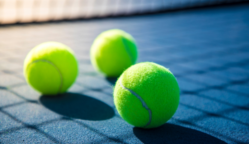 Three yellow tennis balls on a tennis court. 