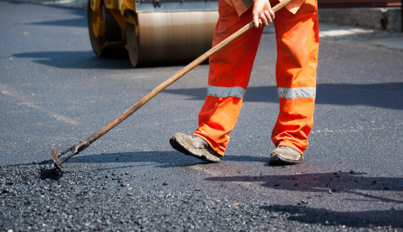 A worker spreading asphalt on a roadway.