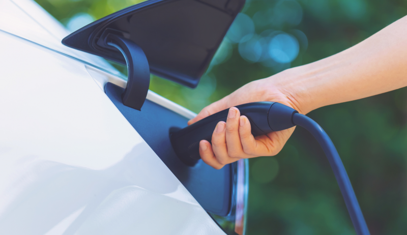 A close-up of a person plugging a charger into an electric vehicle. 