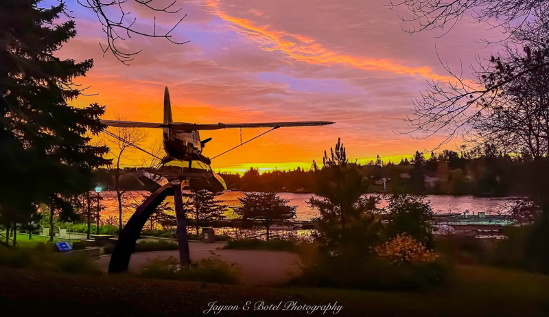 A sunset view of a statue of a plane near a lake and trees